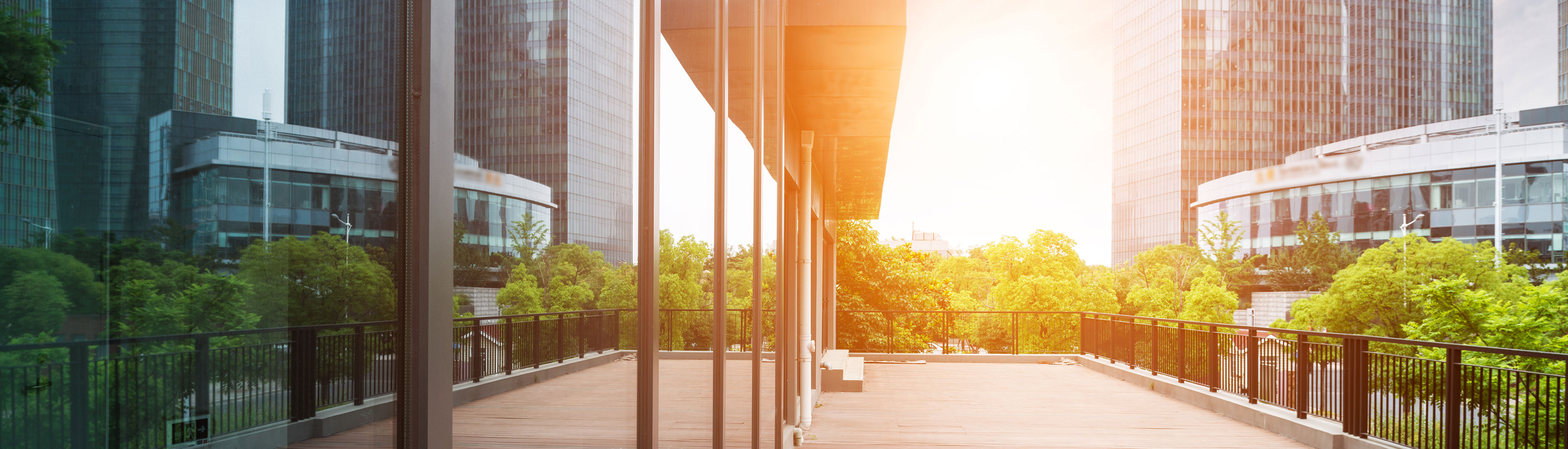 An exterior view of a glass-lined building at sunset, reflecting the surrounding buildings and trees.