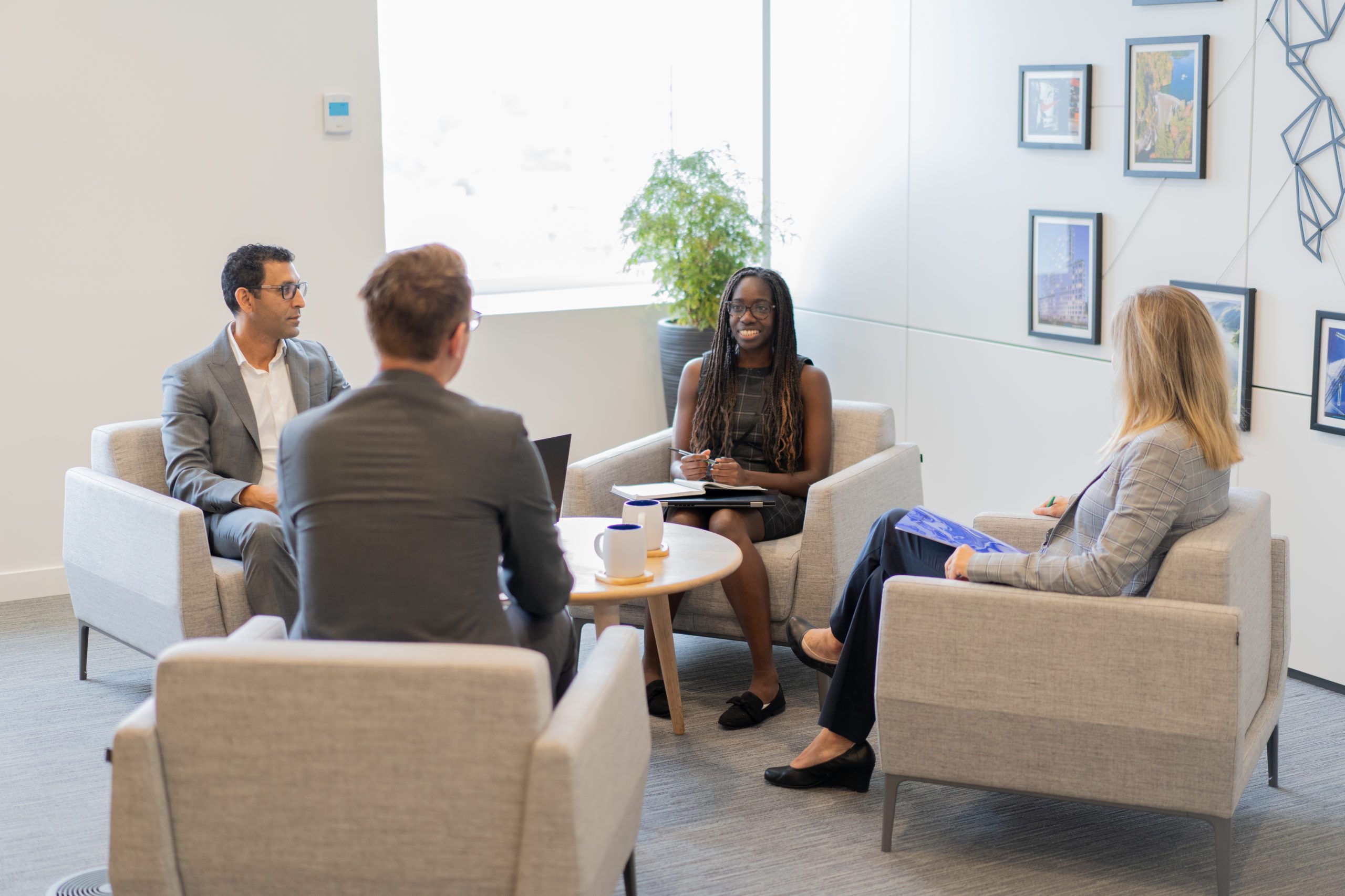 Four BCI employees seated in upholstered armchairs facing each other, with a coffee table in the middle, having a conversation. Four BCI employees seated in upholstered armchairs facing each other, with a coffee table in the middle, having a conversation.