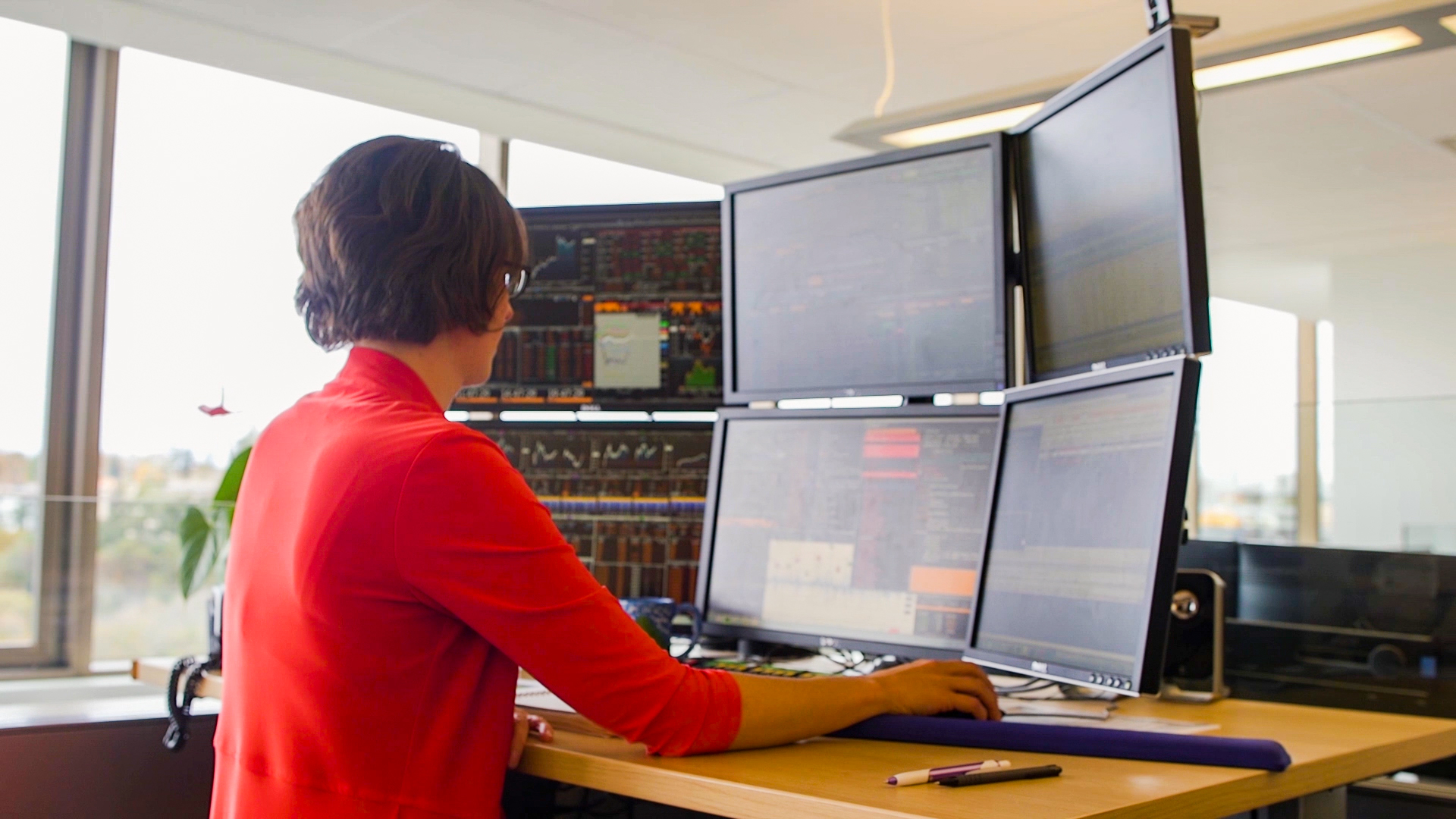 A BCI employee working at a standing desk, looking at an array of six computer monitors. A BCI employee working at a standing desk, looking at an array of six computer monitors.